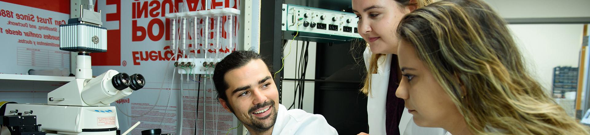 Male and two female students in lab coats looking at lab equipment in a lab